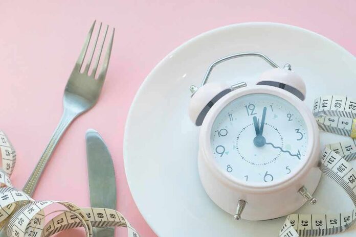 Pink alarm clock on a white plate with fork, knife, and measuring tape