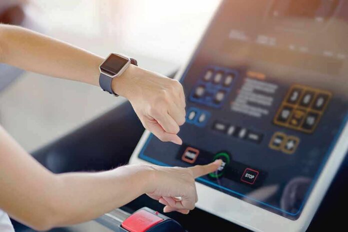 shutterstock_1295291887 Person using a treadmill touchscreen with a smartwatch