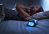 Person lying awake in bed beside a glowing digital alarm clock