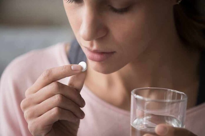 shutterstock_1477334069 Woman holding a white pill and a glass of water