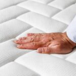 Sleep Essential Checklist for Better Nights Hand pressing a quilted white mattress surface