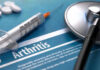 Syringe and stethoscope on arthritis document