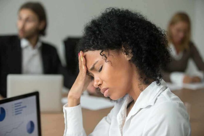 shutterstock_1022439613-2 Woman in office holding her head with eyes closed