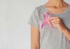 Pink Ribbons Don’t Save Lives Person holding a pink ribbon on a gray shirt