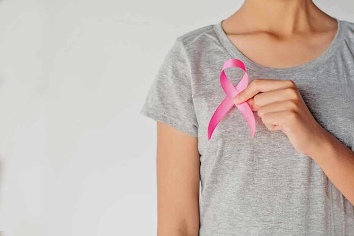 shutterstock_1032241918 Person holding a pink ribbon on a gray shirt