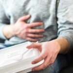 Person holding stomach with takeout container on lap