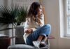 Surgeon General Sounds Alarm On Loneliness Woman sitting curled up on a chair looking out a window