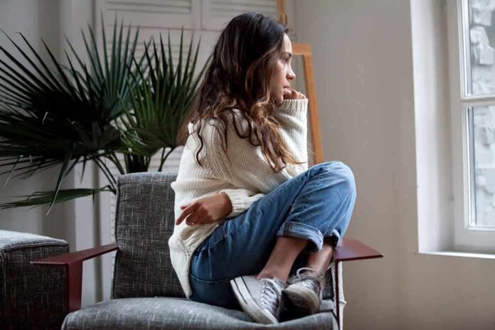 shutterstock_1100199110 Woman sitting curled up on a chair looking out a window