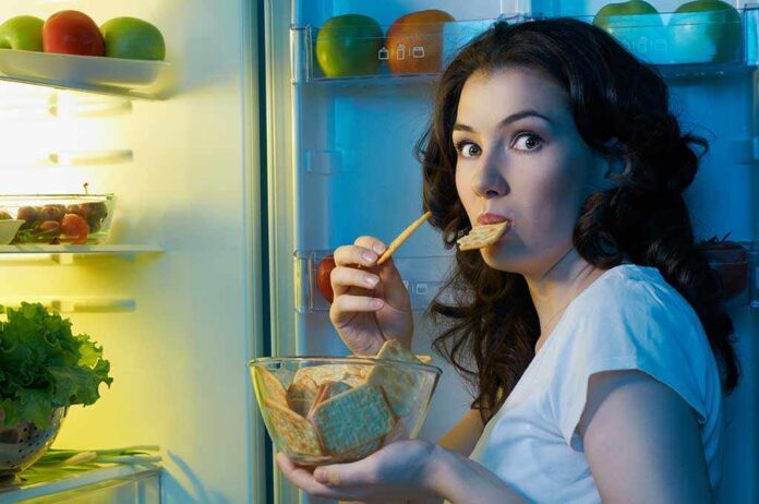 Woman snacking at an open refrigerator