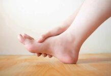 When Does Your Shoe Size Stop Growing? Hand holding the arch of a bare foot on a wooden floor