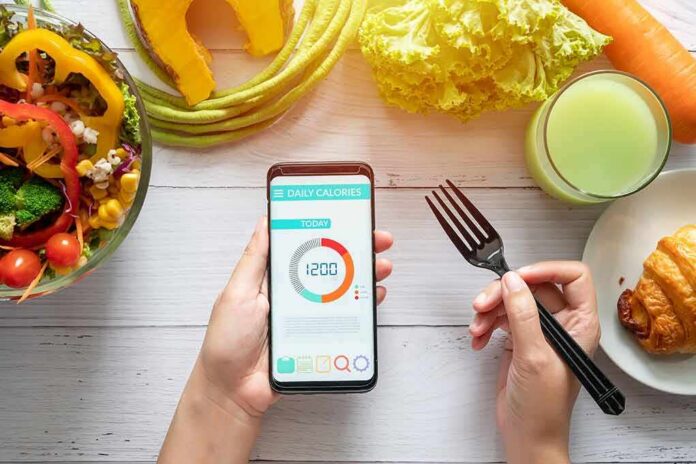 hands holding phone with calorie tracker beside salad and pastry