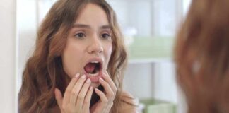 young woman checking inside her mouth in bathroom mirror