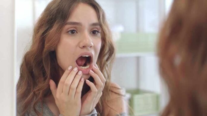 young woman checking inside her mouth in bathroom mirror