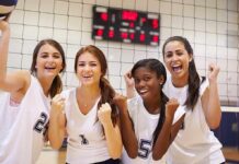 Four female volleyball players celebrating in a gymnasium