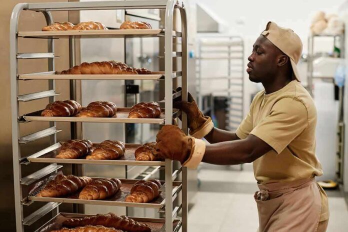 shutterstock_2373543347 Baker moving a rack of freshly baked braided loaves