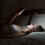 Bedroom Glow Tied To Heart Danger Woman lying in bed looking at smartphone