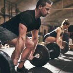 Build Muscle, Lose Fat—Same Workout? Man deadlifting a barbell in a gym with a woman lifting behind him