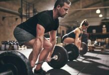 Man deadlifting a barbell in a gym with a woman lifting behind him