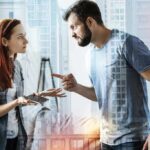 Two adults arguing indoors, man pointing at woman holding a phone