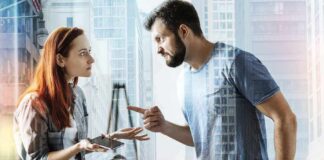 Two adults arguing indoors, man pointing at woman holding a phone