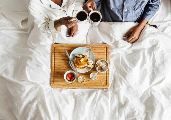 Breakfast in bed with two people holding coffee