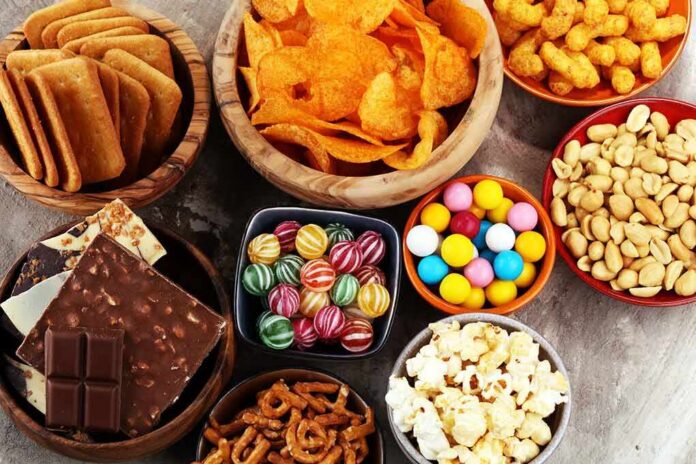 Assorted snacks in bowls including chips, candies, nuts, popcorn, and chocolate
