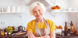 Smiling older woman in apron standing in a bright kitchen