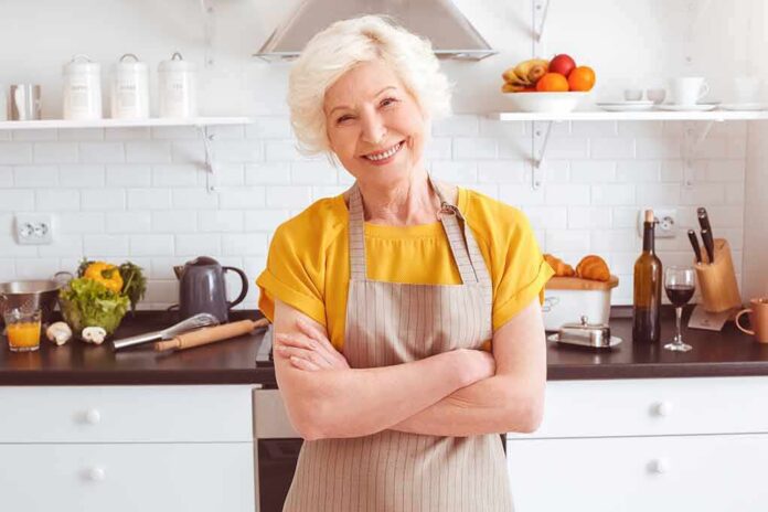 shutterstock_1063660049 Smiling older woman in apron standing in a bright kitchen