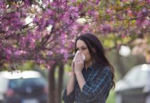 Flu Surge Looms – CDC’s Unpopular Fix Woman sneezing into tissue under blooming pink trees