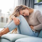 Silent IBD Flags That Emerge Years Early Woman holding her stomach in pain on a sofa