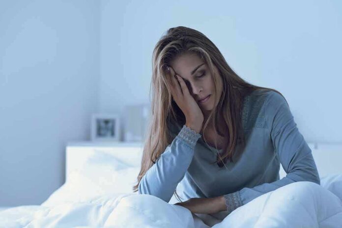 Woman sitting in bed looking tired with hand on face