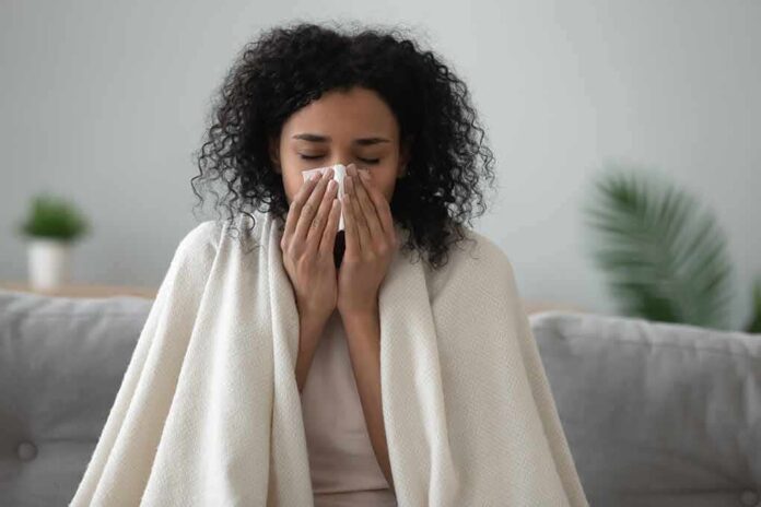 shutterstock_1444224857 Woman wrapped in a blanket blowing her nose