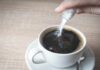 Sugar Supercharges Antibiotic Damage hand pouring sugar into a cup of black coffee