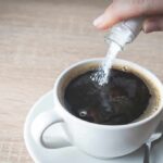 Sugar Supercharges Antibiotic Damage hand pouring sugar into a cup of black coffee