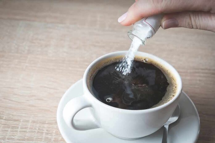 hand pouring sugar into a cup of black coffee