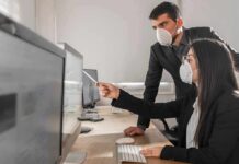 Two office workers wearing masks at a computer