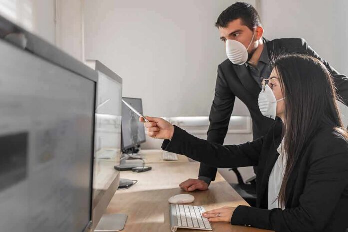 Two office workers wearing masks at a computer