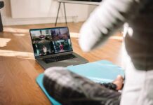 person on yoga mat watching a virtual workout class on a laptop