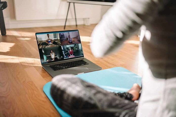 shutterstock_1708844755 person on yoga mat watching a virtual workout class on a laptop