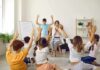 Therapist Blasts ‘Gentle Parenting’ Trend Children raise hands in a classroom circle with teacher clapping