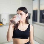 WHO Warning: Stop Chasing Protein Powders Woman in sportswear drinking a smoothie in a kitchen