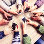 The science of how social media affects mental health Hands around a table holding smartphones