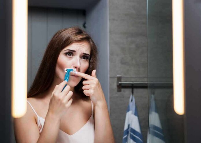 shutterstock_461658664-1 Woman shaving upper lip in bathroom mirror
