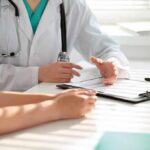 Autoimmune Mystery: Why Women Get Hit Harder Doctor discusses medical notes with patient at a desk