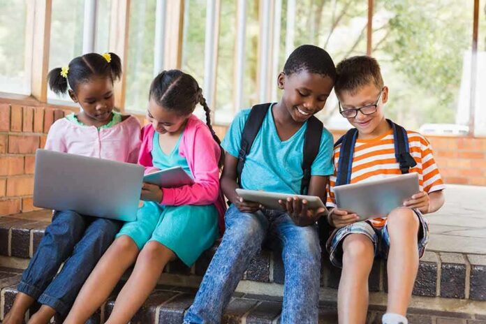 shutterstock_574060864 Children using laptops and tablets on school steps