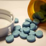 Cardiovascular Risks of Using Adderall Recreationally Blue pills spilled from an orange prescription bottle beside a white cap