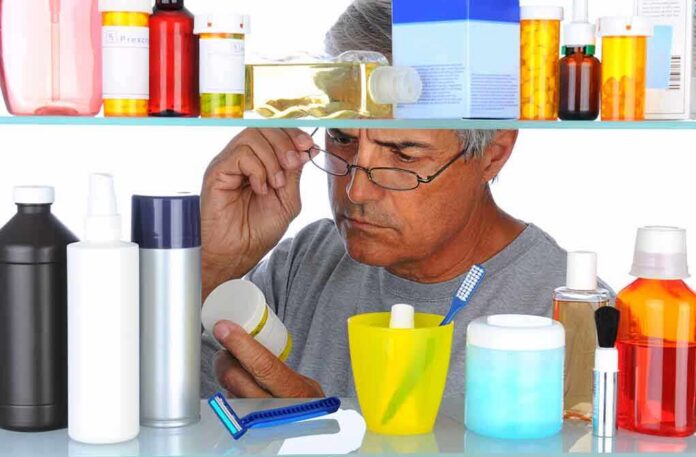 Man reading a pill bottle in a bathroom cabinet